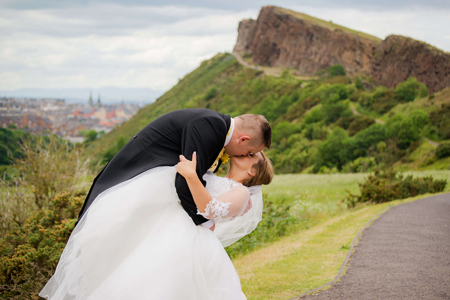 Bride and groom sharing a kiss outdoors with dramatic hillside scenery, coordinated by DSW Weddings
