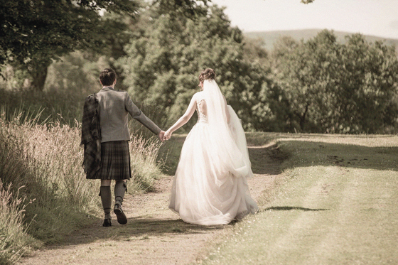 Bride and groom walking hand in hand along a rural path following their wedding day, planned by DSW Weddings