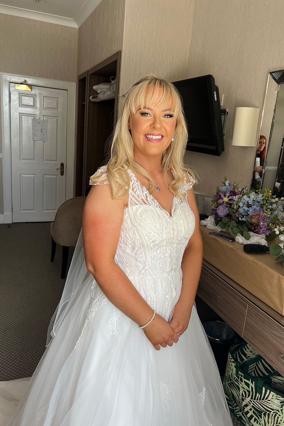 Blonde bride smiling in a lace wedding dress with natural, radiant bridal makeup by Hannah Inglis Beauty
