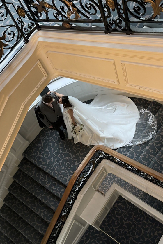 Bride and groom walking down grand staircase together, veil flowing behind in elegant hotel wedding setting