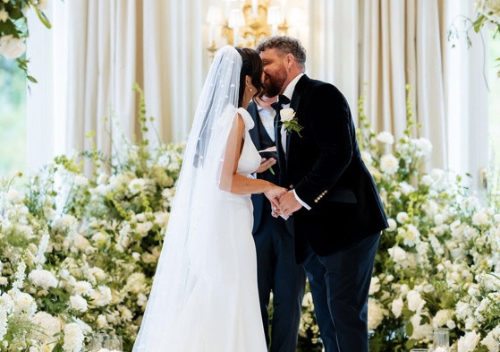 Bride and groom sharing a kiss during their wedding ceremony at Turnberry, framed by large-scale white floral installations and soft candlelight in an elegant Scottish venue.
