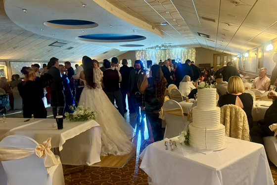 Bride and guests on the dancefloor beside a tiered wedding cake during a lively Scottish wedding reception