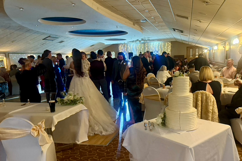 Bride and guests on the dancefloor beside a tiered wedding cake during a lively Scottish wedding reception