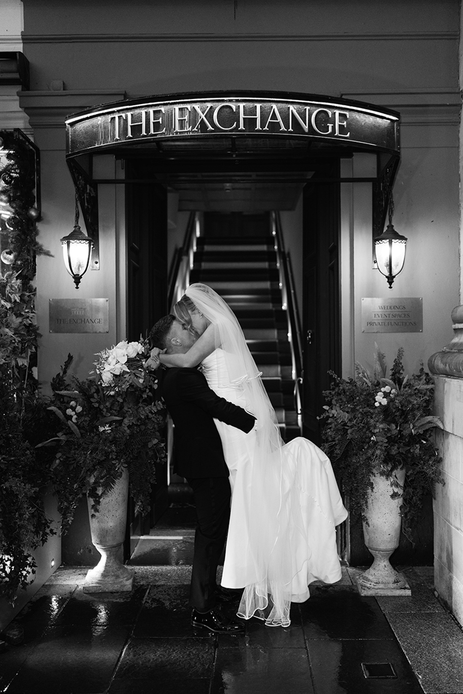 Groom lifting bride for kiss outside The Exchange entrance black and white city wedding photo