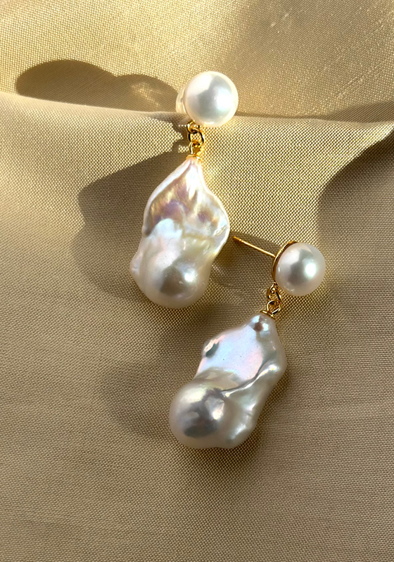 Baroque pearl drop earrings with gold stud detail on neutral fabric background