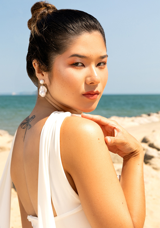 Bride on beach wearing baroque pearl drop earrings, hair in bun, coastal bridal look