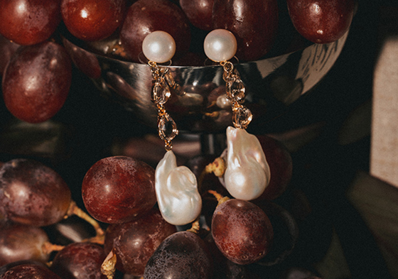 Pearl and gold drop earrings styled against red grapes in editorial jewellery shoot