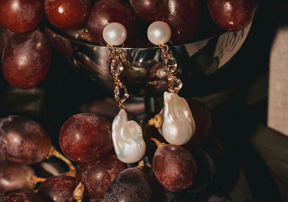 Pearl and gold drop earrings styled against red grapes in editorial jewellery shoot