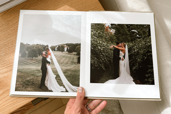 Hand holding a luxury Inkifi wedding photo album open to romantic outdoor wedding portraits of the bride and groom