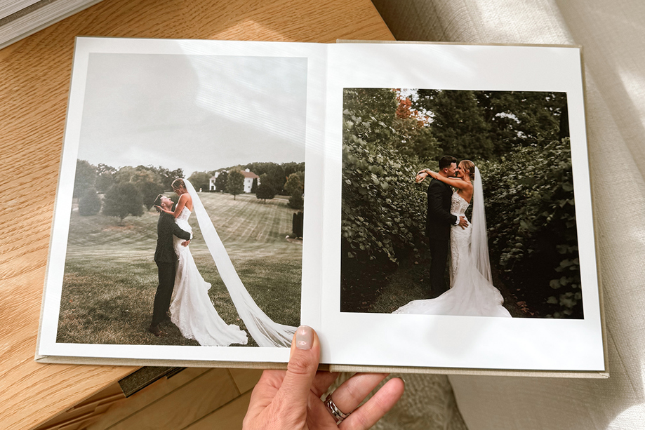 Hand holding a luxury Inkifi wedding photo album open to romantic outdoor wedding portraits of the bride and groom