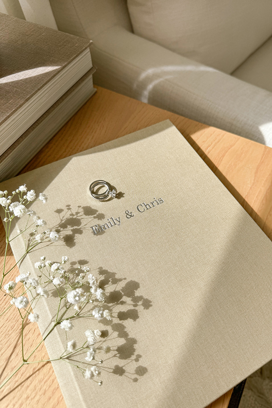 Premium linen wedding photo album by Inkifi with wedding rings and gypsophila styled on a wooden table in natural light