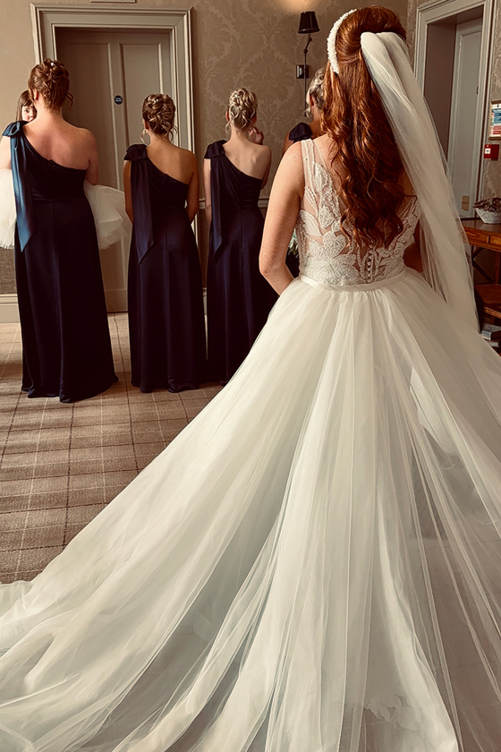 Bride in lace wedding dress revealing her bridal look to bridesmaids during wedding morning preparations captured by Effortless Ivory Weddings