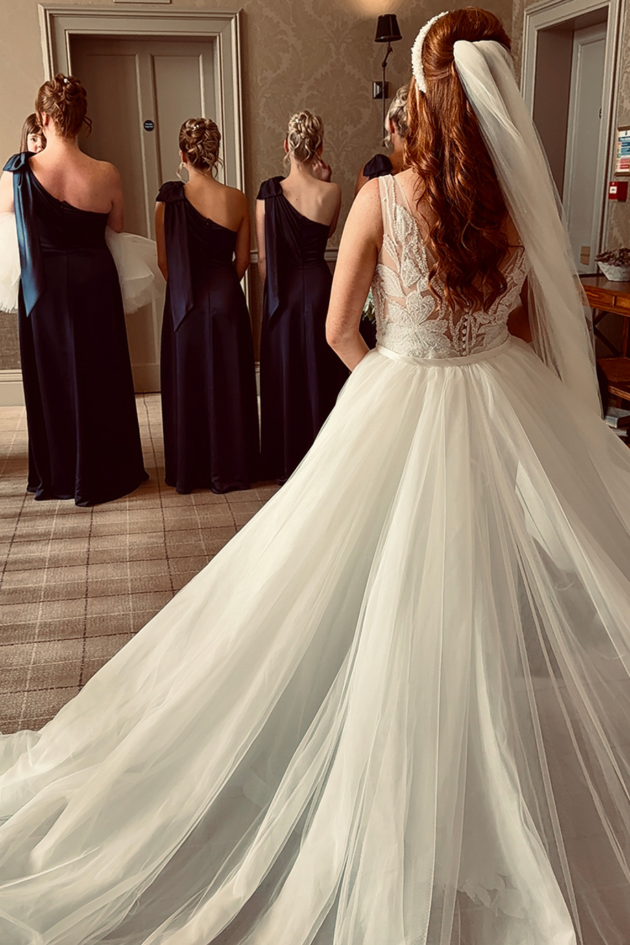Bride in lace wedding dress revealing her bridal look to bridesmaids during wedding morning preparations captured by Effortless Ivory Weddings