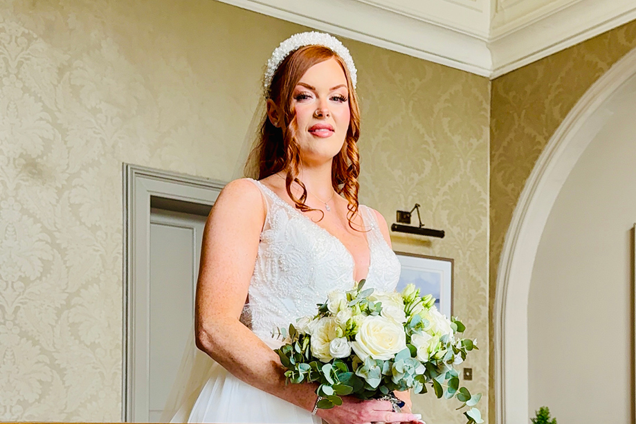 Bride wearing a pearl headband and lace wedding dress holding a white rose bouquet during bridal prep captured by Effortless Ivory Weddings
