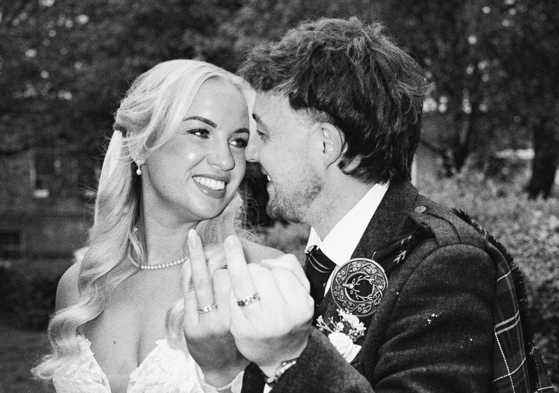 Black and white wedding content image of bride and groom laughing together while showing their wedding rings