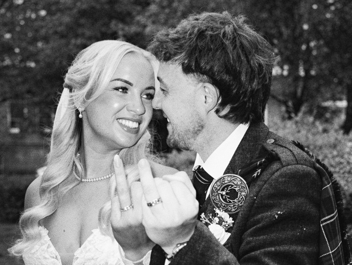 Black and white wedding content image of bride and groom laughing together while showing their wedding rings