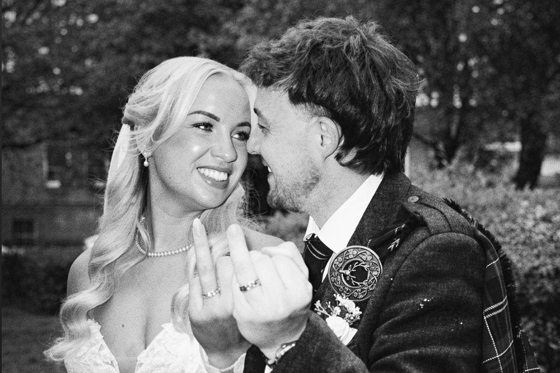 Black and white wedding content image of bride and groom laughing together while showing their wedding rings