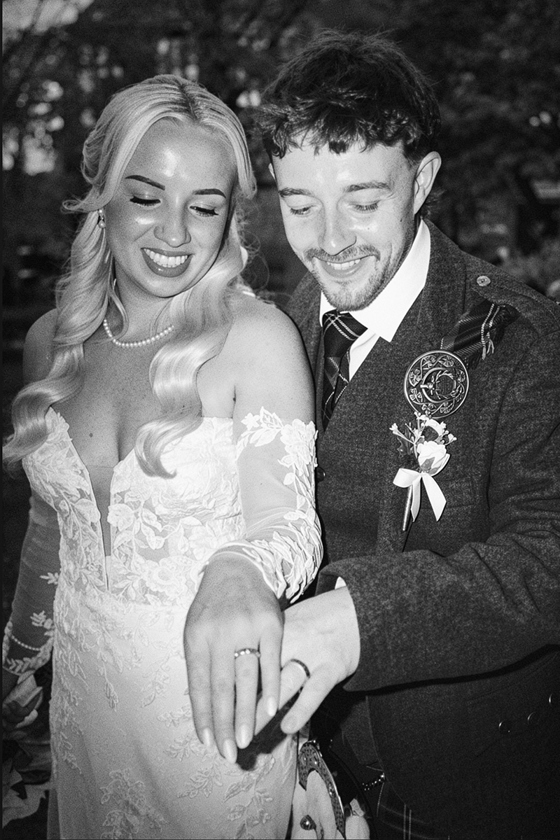 Black and white wedding content image of bride and groom smiling and showing their wedding rings