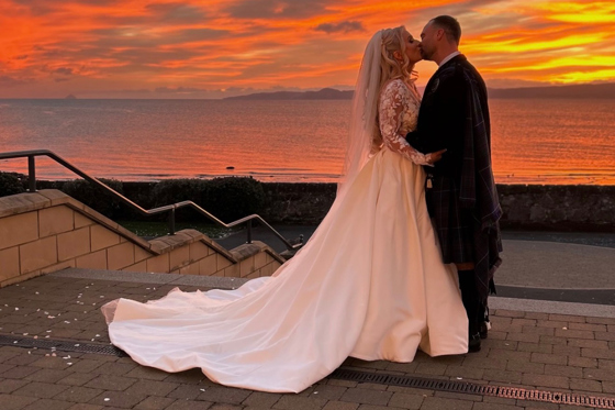 Bride and groom kissing by the sea at sunset in a romantic wedding content image by Arauthentic Moments