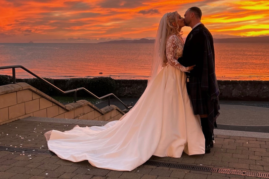 Bride and groom kissing by the sea at sunset in a romantic wedding content image by Arauthentic Moments