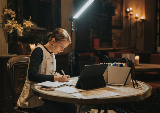 Colleen creating live wedding illustrations during an evening reception with drawing materials and lighting setup.