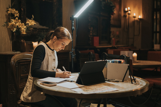 Colleen creating live wedding illustrations during an evening reception with drawing materials and lighting setup.
