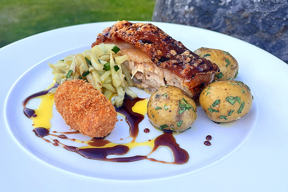 Plated pork dish with potatoes, vegetables and croquette served by Wylie & Wood as part of a luxury catering menu.