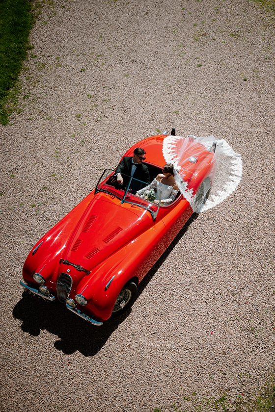 Aerial wedding photo of bride and groom in a red vintage car by Kamila Pickles Photography