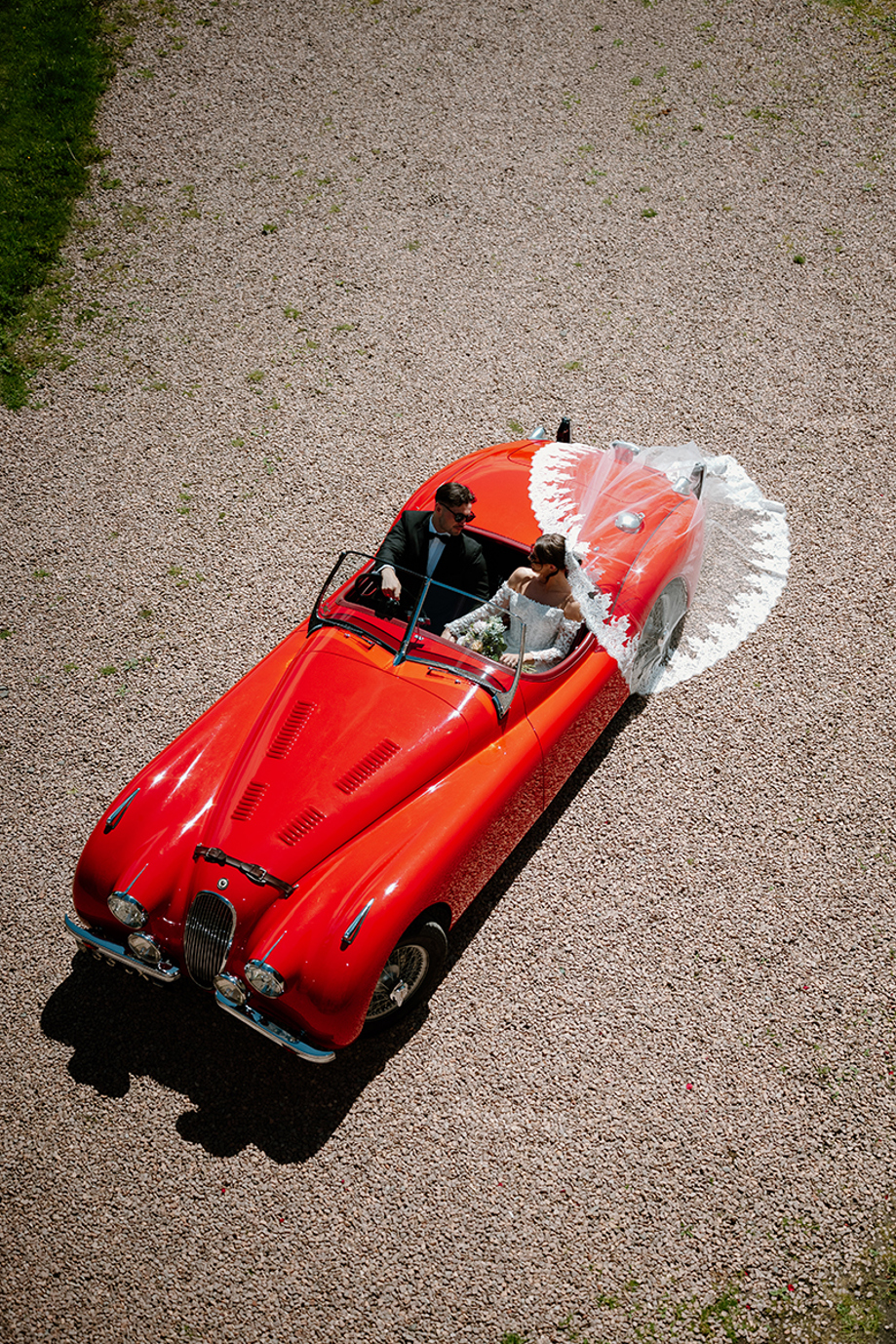 Aerial wedding photo of bride and groom in a red vintage car by Kamila Pickles Photography