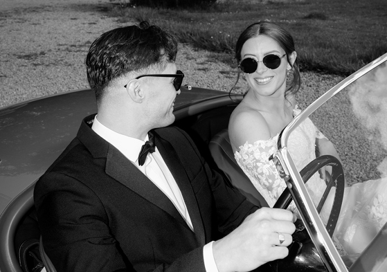 Black and white wedding portrait of bride and groom in a vintage car by Kamila Pickles Photography