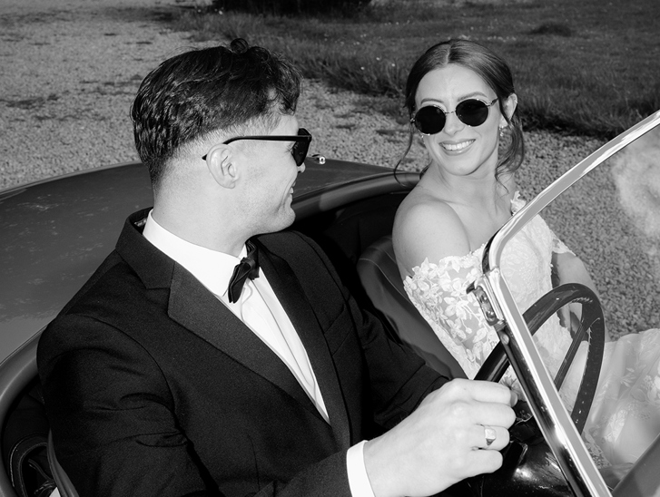 Black and white wedding portrait of bride and groom in a vintage car by Kamila Pickles Photography