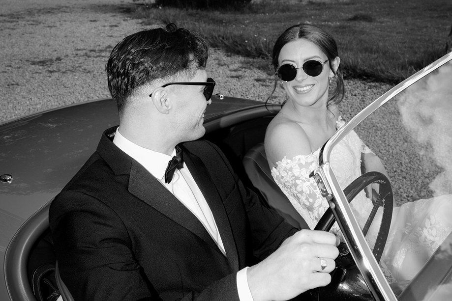 Black and white wedding portrait of bride and groom in a vintage car by Kamila Pickles Photography
