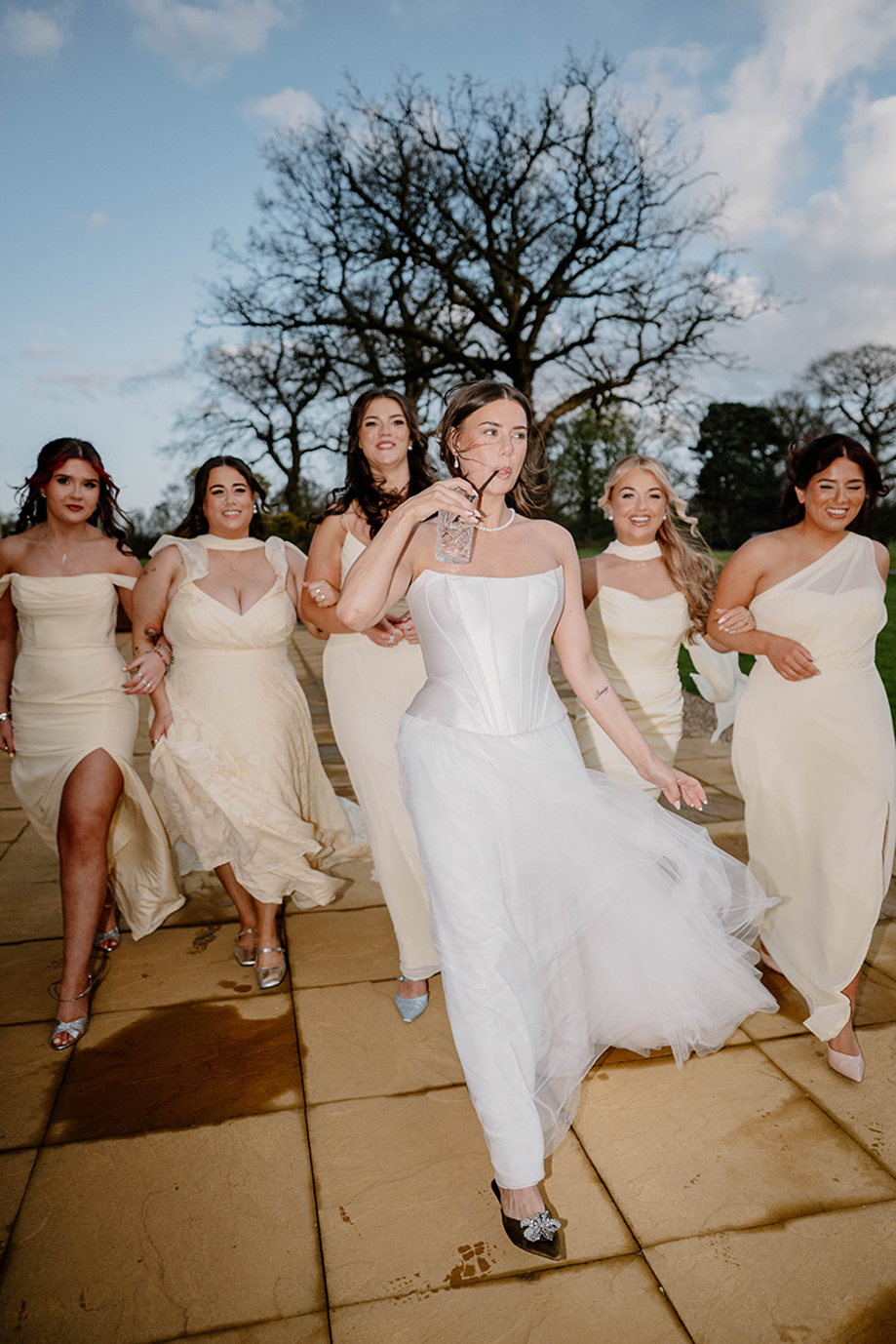 Bride and bridesmaids in cream dresses walking outdoors on a wedding day by Kamila Pickles Photography