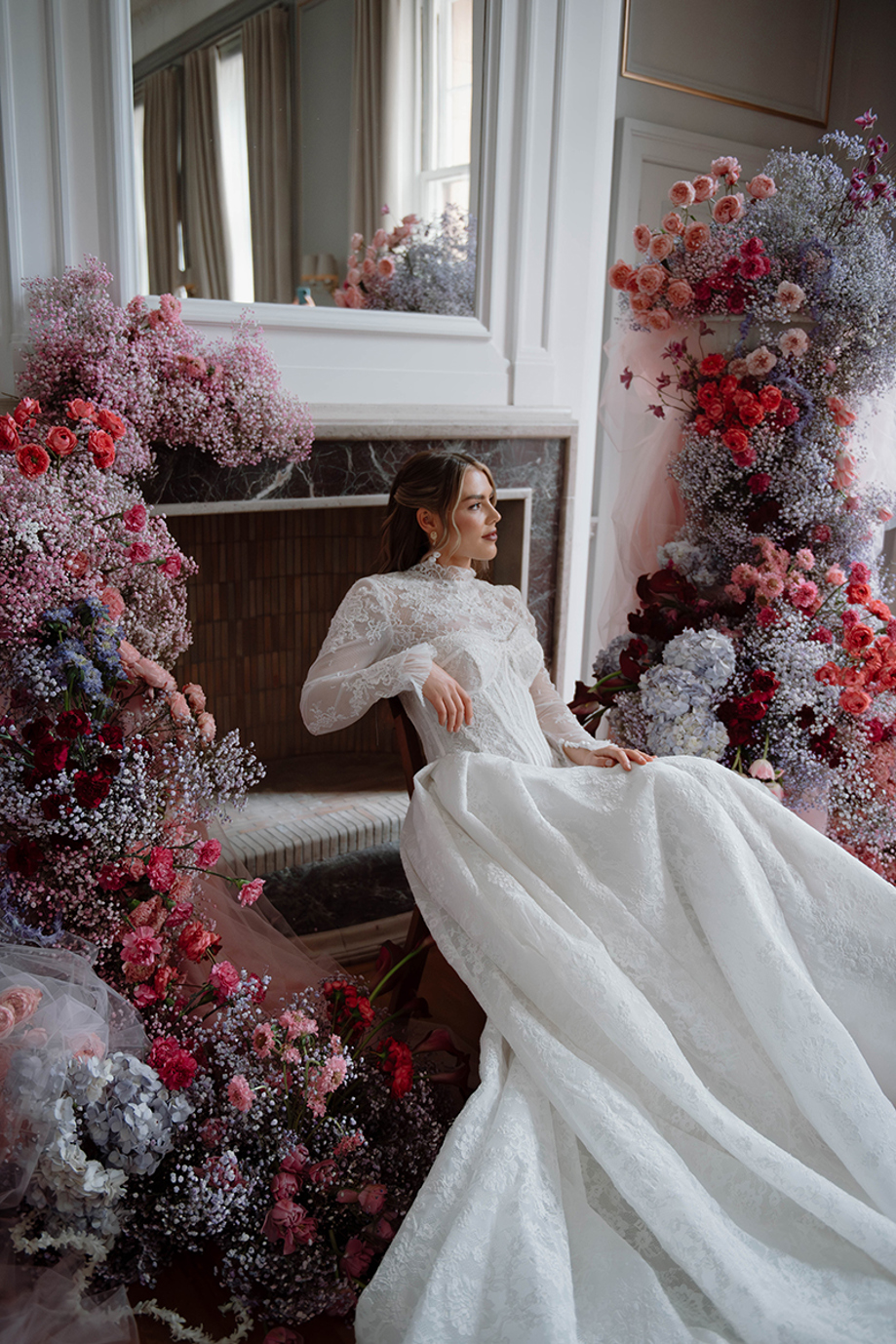 Bride in lace wedding dress seated beside colourful floral installations by Kamila Pickles Photography