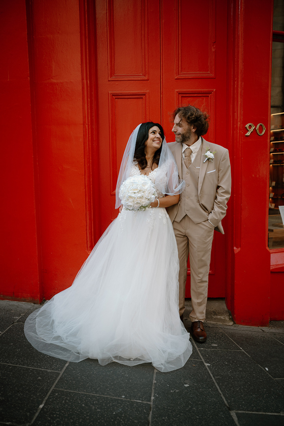 Wedding couple posing in front of bold red doors during city wedding portraits by Kamila Pickles Photography
