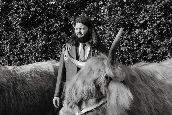 Harris Highlanders groom in kilt posing with a Highland cow at a Scottish wedding