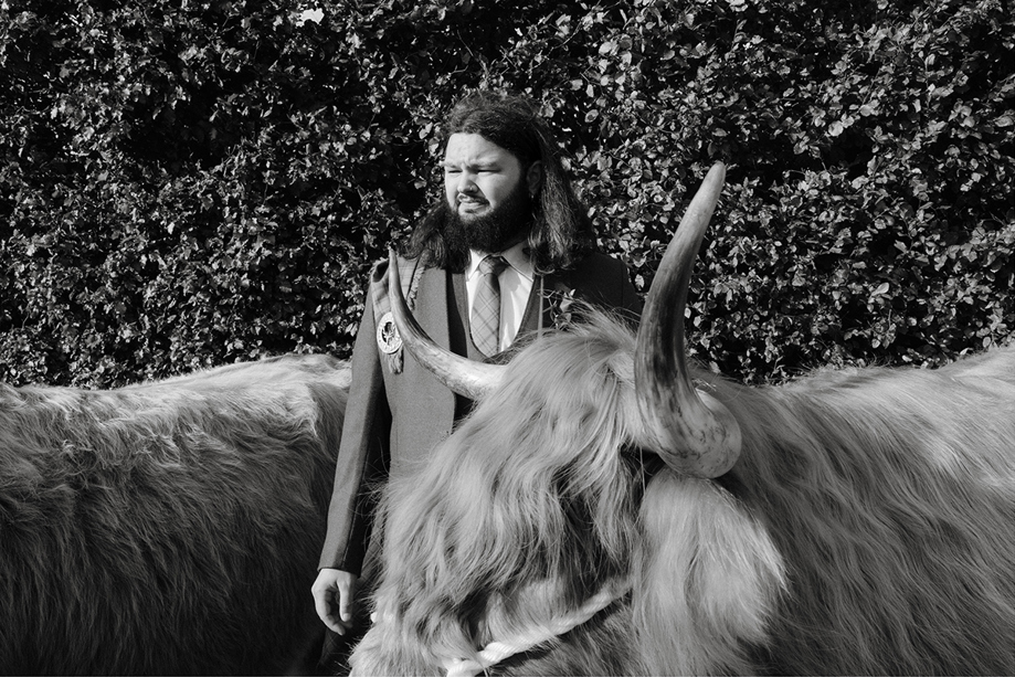 Harris Highlanders groom in kilt posing with a Highland cow at a Scottish wedding