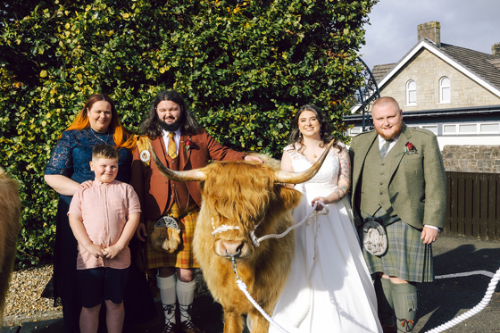 Wedding couple and family posing with a Harris Highlanders Highland cow