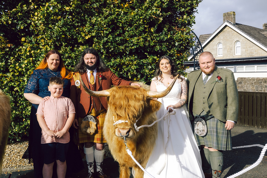 Wedding couple and family posing with a Harris Highlanders Highland cow