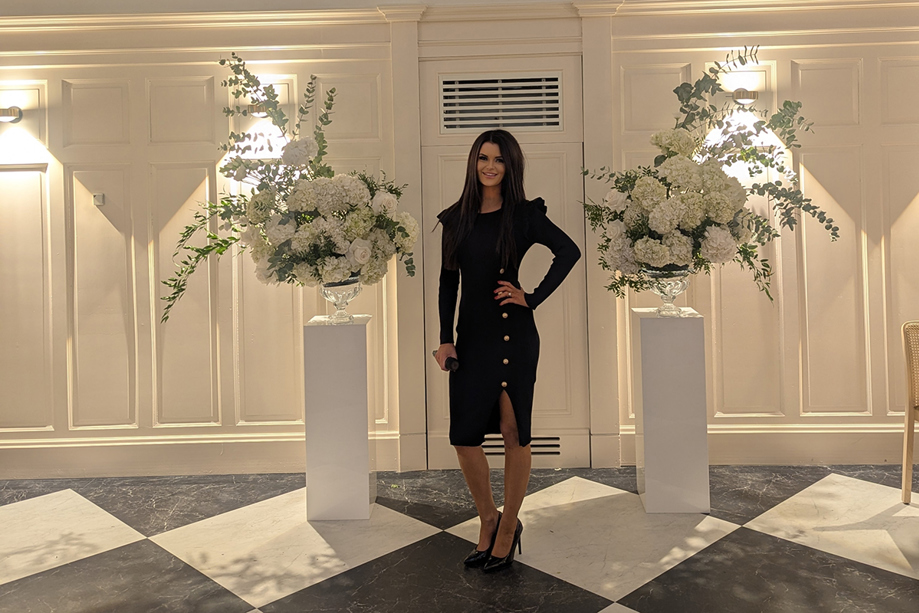 Vocals by Suzie standing in an elegant wedding venue with white floral arrangements and arched windows