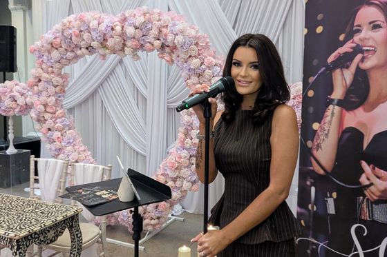 Vocals by Suzie at a wedding showcase with microphone, pink floral arch and branded display banner