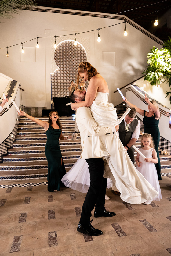 Groom lifts and kisses the bride on the dance floor as wedding guests celebrate around them.