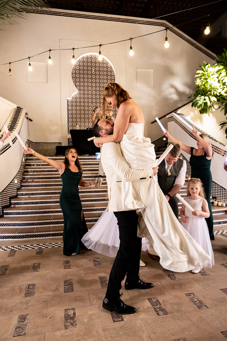 Groom lifts and kisses the bride on the dance floor as wedding guests celebrate around them.