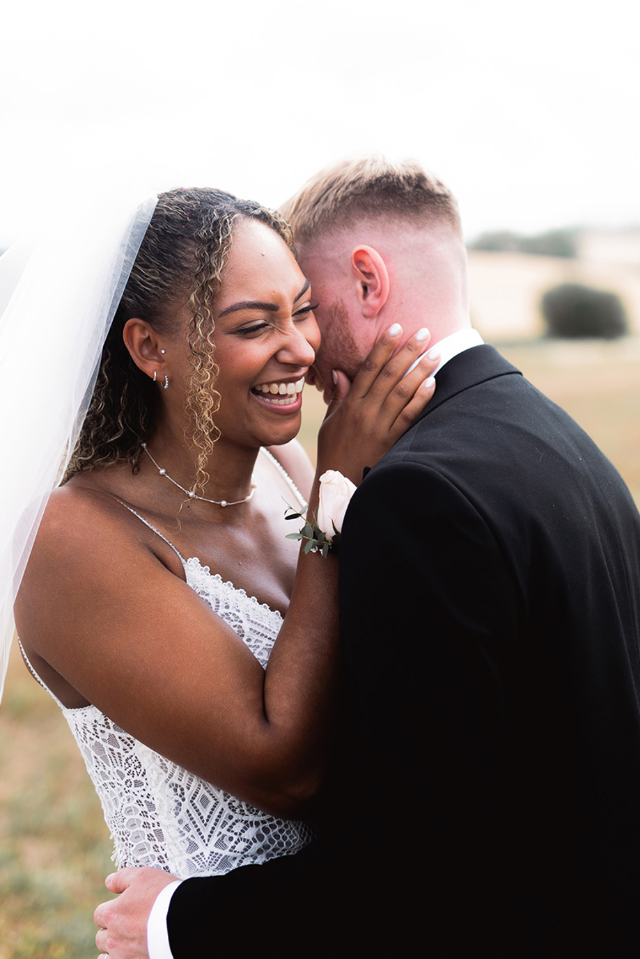 Laughing bride embraces the groom during a relaxed outdoor wedding portrait in the countryside.