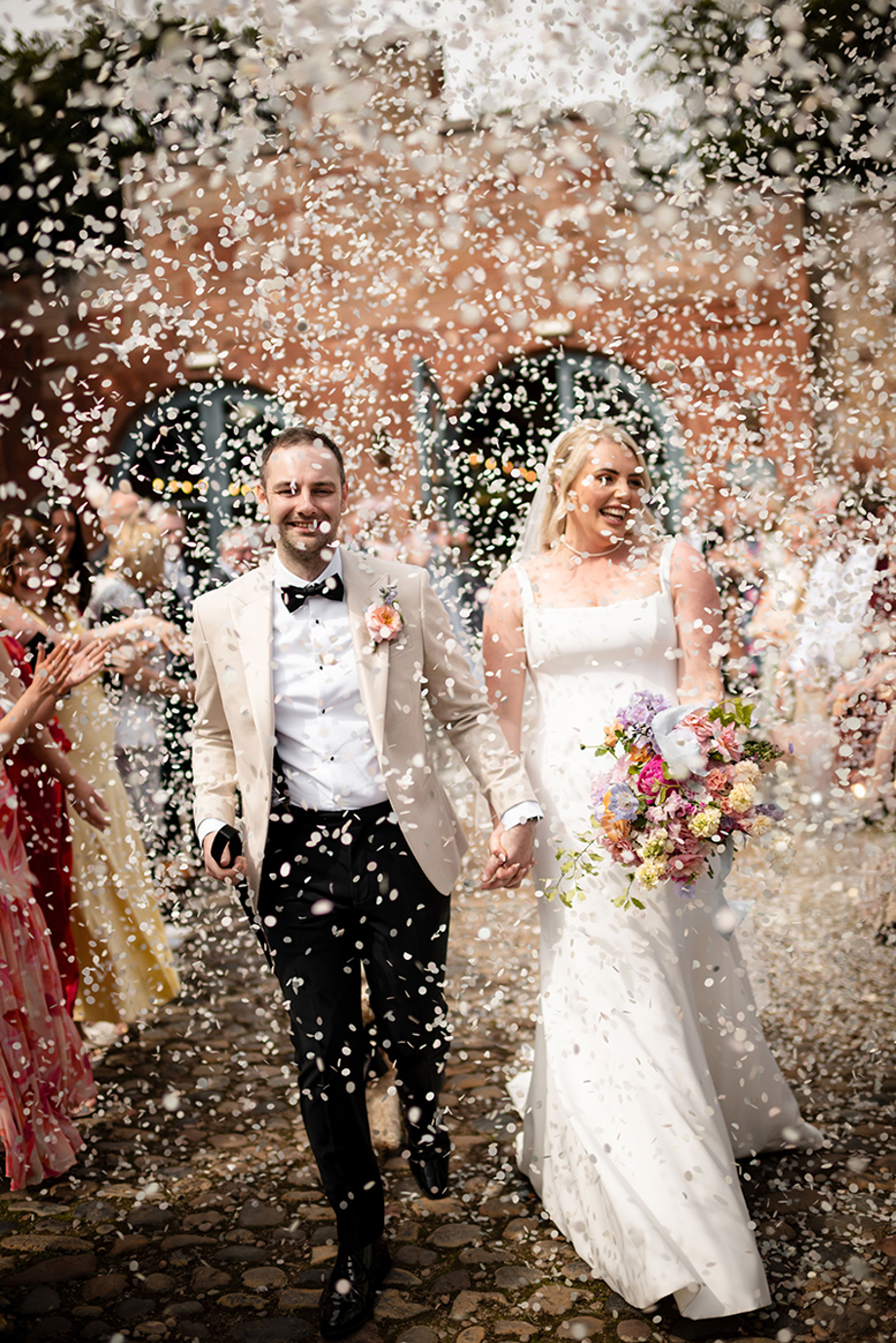 Bride and groom walk through confetti with colourful wedding bouquet by Agapanthus Flower Studio