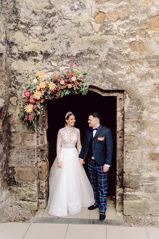 Newlyweds beneath a bright floral doorway installation by Agapanthus Flower Studio at Dundas Castle
