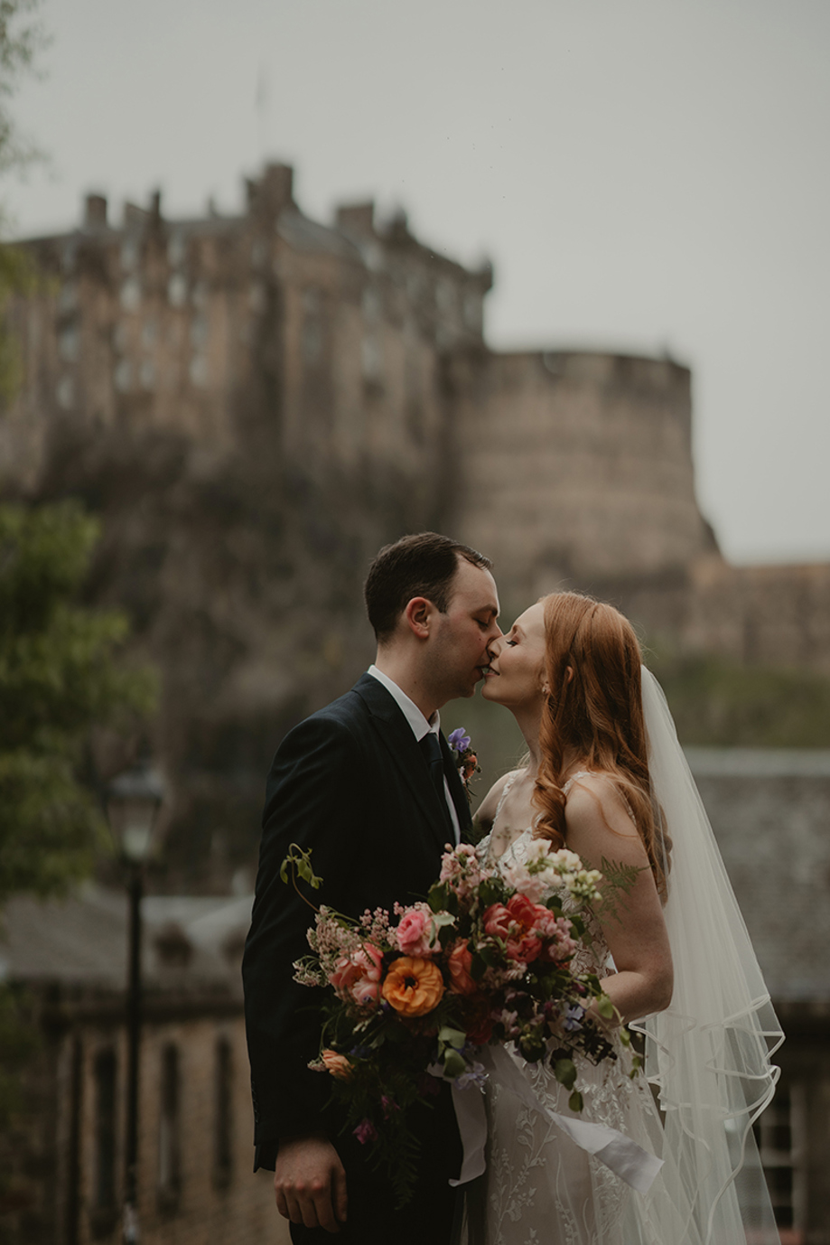 Bride and groom kiss with colourful bridal bouquet and castle backdrop in Scotland