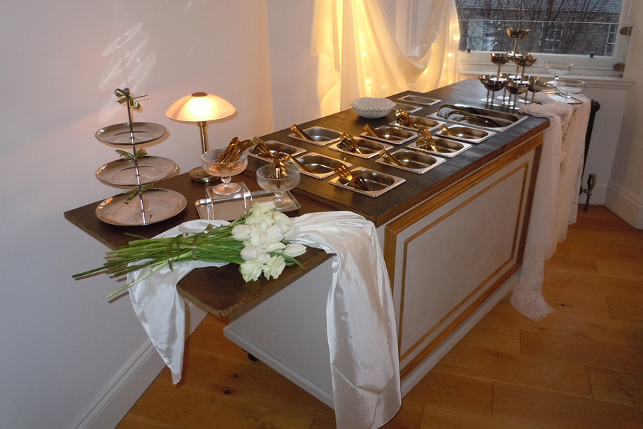 Bramble & Brie indoor wedding grazing cart with gold serving dishes, white flowers and warm ambient lighting
