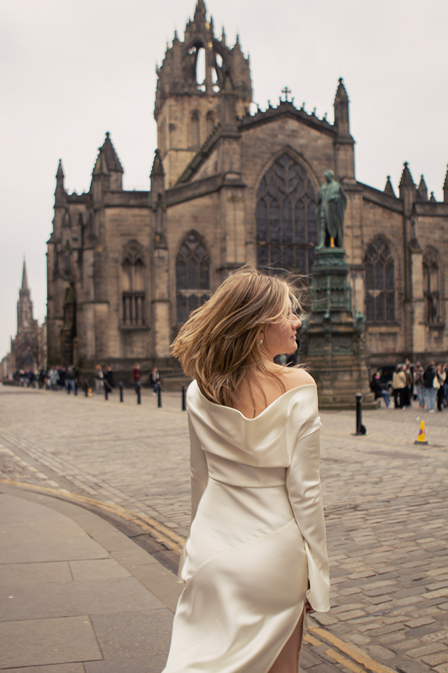 Bride in a satin wedding dress walking along Edinburgh’s Royal Mile with St Giles’ Cathedral in the background, photographed by RScott_shoots.