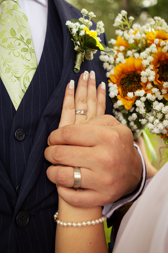 Close-up of a newlywed couple showing their wedding rings beside a sunflower bridal bouquet, captured by Rscott_shoots.